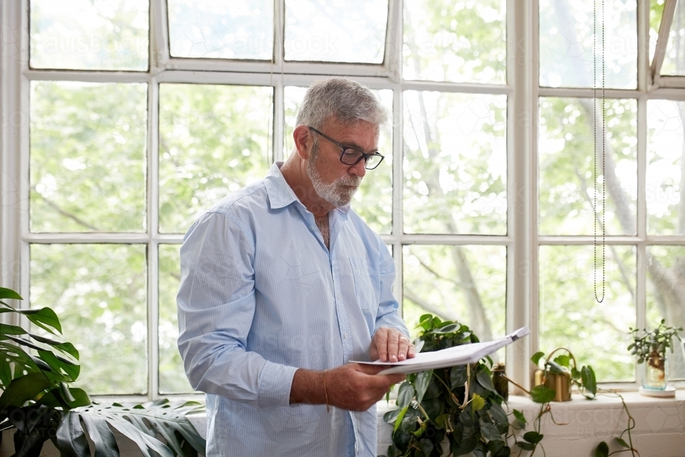 Horizontal shot of a man standing behind a window while holding his files. - Australian Stock Image