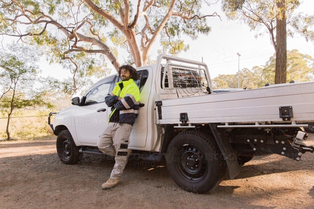 horizontal shot of a man with curly hair wearing neon jacket standing against a white pick up truck - Australian Stock Image