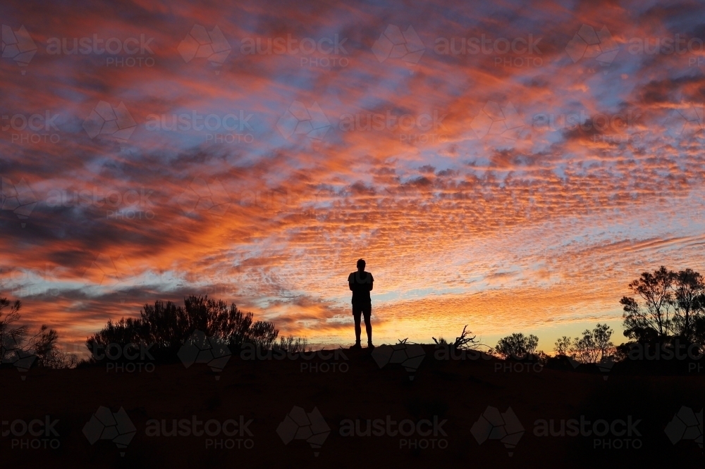 silhouetted person standing on a hilltop at sunset. - Australian Stock Image