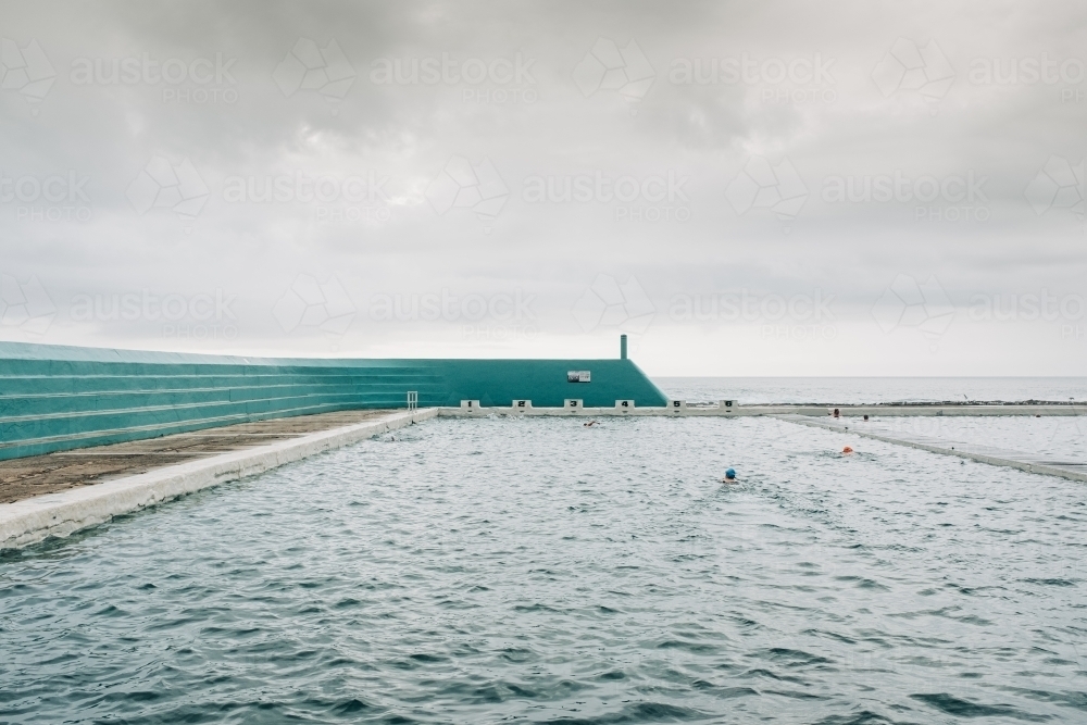 horizontal shot of a person swimming in a large ocean pool on a cloudy day - Australian Stock Image