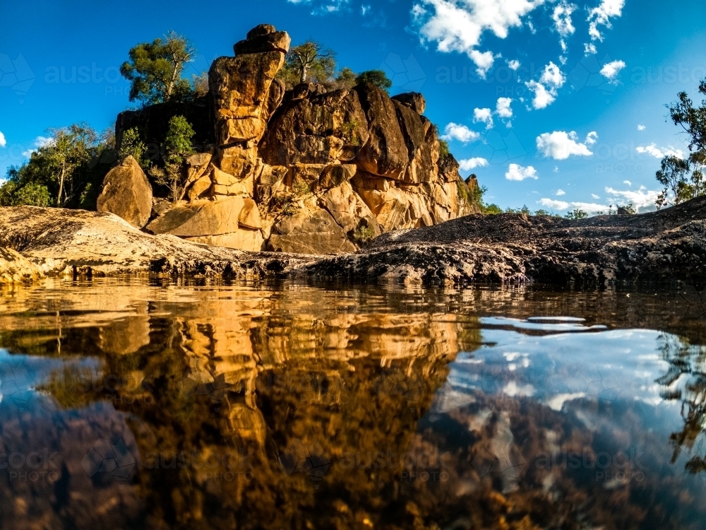 Horizontal shot of a reflection of rocks in water on a cloudy blue sky - Australian Stock Image
