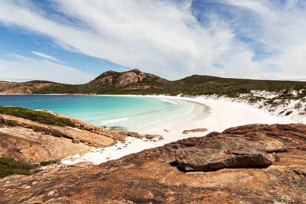 Horizontal shot of a remote white sand beach with mountains on a sunny day with blue and white skies - Australian Stock Image