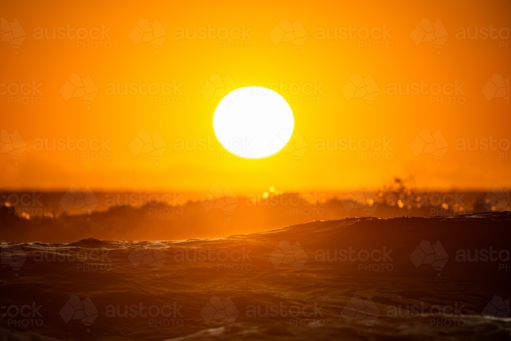 Horizontal shot of a rising sun above the ocean waves at sunrise - Australian Stock Image