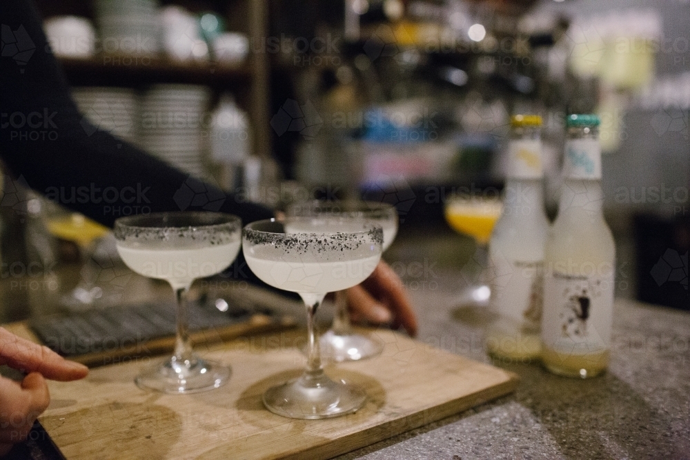Horizontal shot of a server's hand serving a tray of cocktails. - Australian Stock Image
