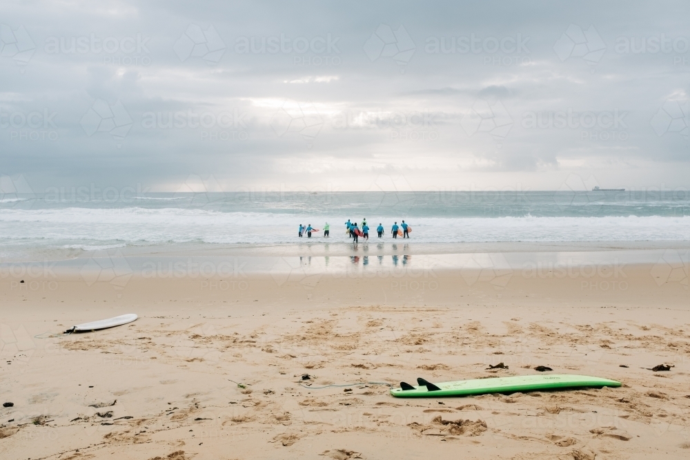 horizontal shot of a shoreline with two surfboards and nine people standing on the sea water - Australian Stock Image