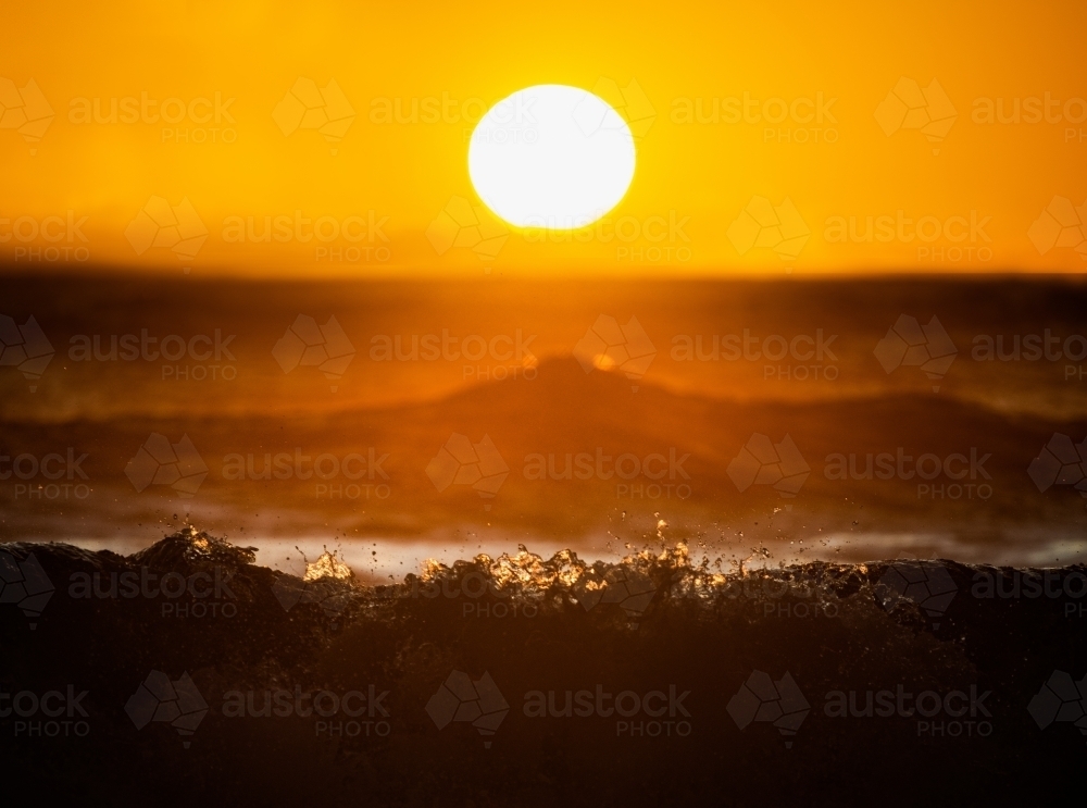 Horizontal shot of a sun above the ocean waves crashing into the water at sunrise - Australian Stock Image