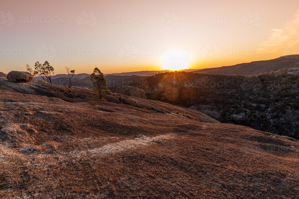 horizontal shot of a sunset on a mountain top with rock, trees and bushes - Australian Stock Image