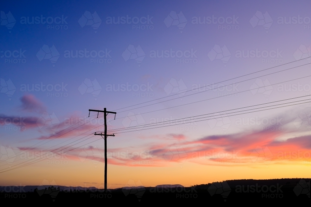horizontal shot of a sunset with a silhouette of an electrical post with wires - Australian Stock Image