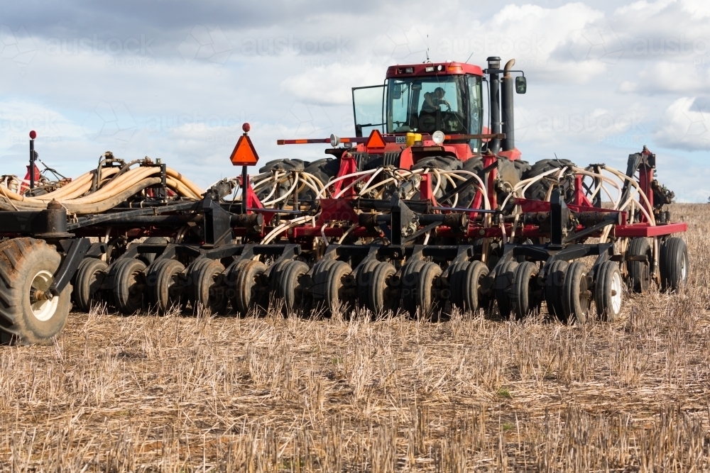 horizontal shot of a tractor plowing soil with cultivator smashing  clods beds on a sunny day - Australian Stock Image