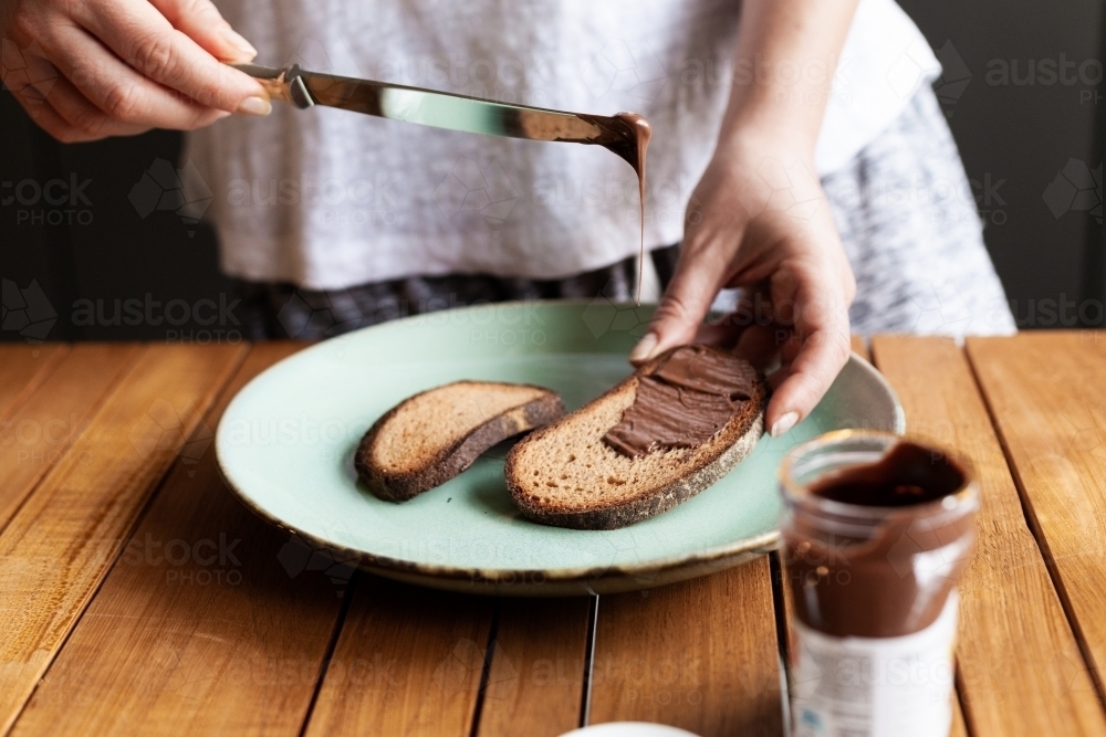 Horizontal shot of a woman spreading chocolate on a toast - Australian Stock Image