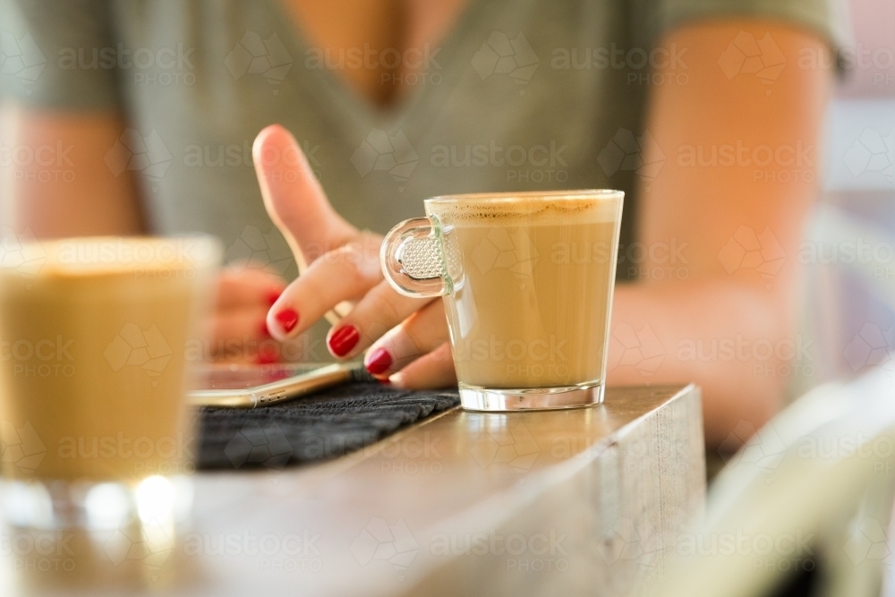 Horizontal shot of a woman using her cellphone with red nails with a cup of coffee on the table - Australian Stock Image