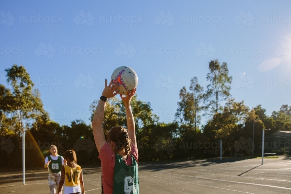 horizontal shot of a young woman holding a net ball with two girls in front on a sunny day - Australian Stock Image