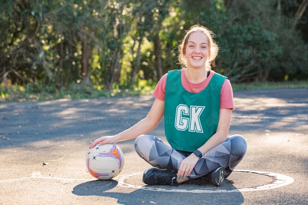 horizontal shot of a young woman sitting on the ground while touching a net ball on a sunny day - Australian Stock Image