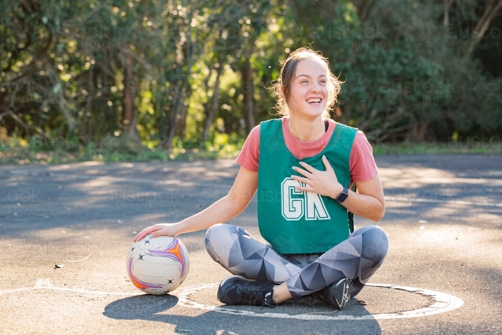 horizontal shot of a young woman sitting on the ground with one hand placed on top of a net ball - Australian Stock Image