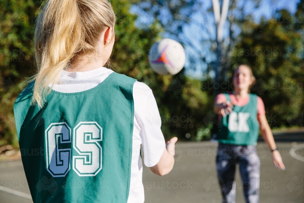 horizontal shot of a young woman throwing a netball and the other catching it on a sunny day - Australian Stock Image