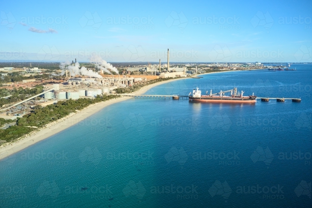 horizontal shot of Kwinana alumina refinery on a sunny day with white smoke, bushes and docked ship - Australian Stock Image
