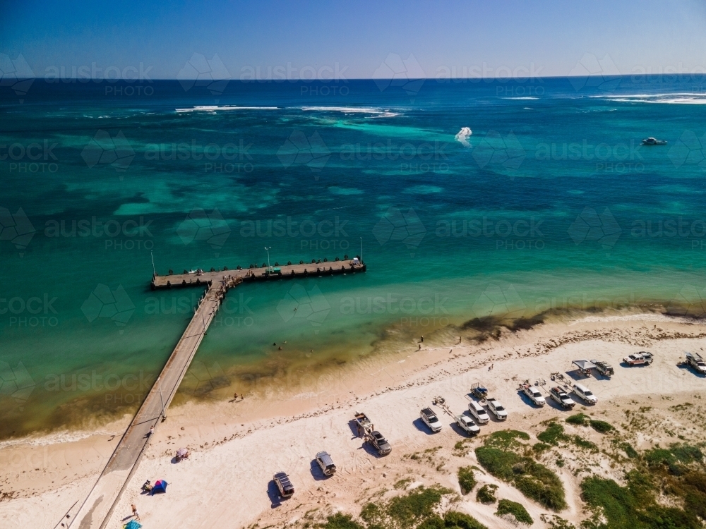 horizontal shot of cars and boats parked on a white sand with bushes, waves and wooden beach walkway - Australian Stock Image