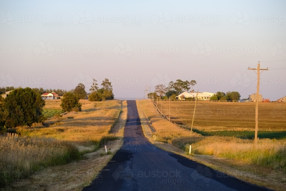 horizontal shot of long narrow outback road with houses and electrical posts on a sunny day - Australian Stock Image