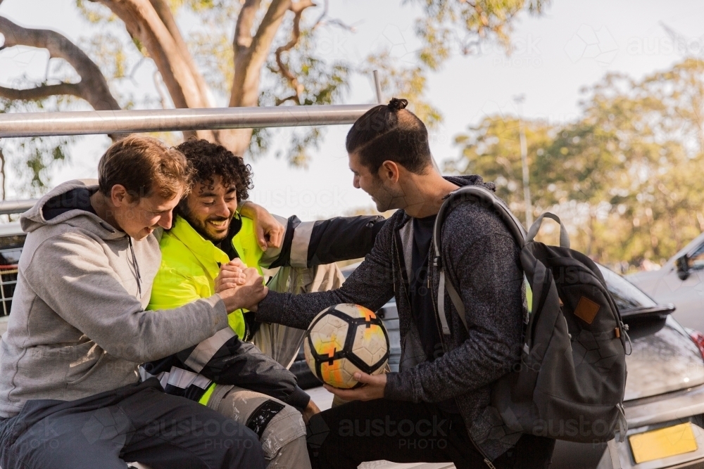 horizontal shot of men with one holding a soccer ball and two shaking hands all in casual clothes - Australian Stock Image
