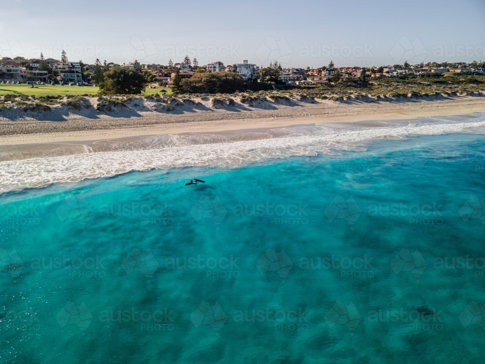 horizontal shot of  ocean water with waves white sand shores, trees, buildings on a sunny day - Australian Stock Image