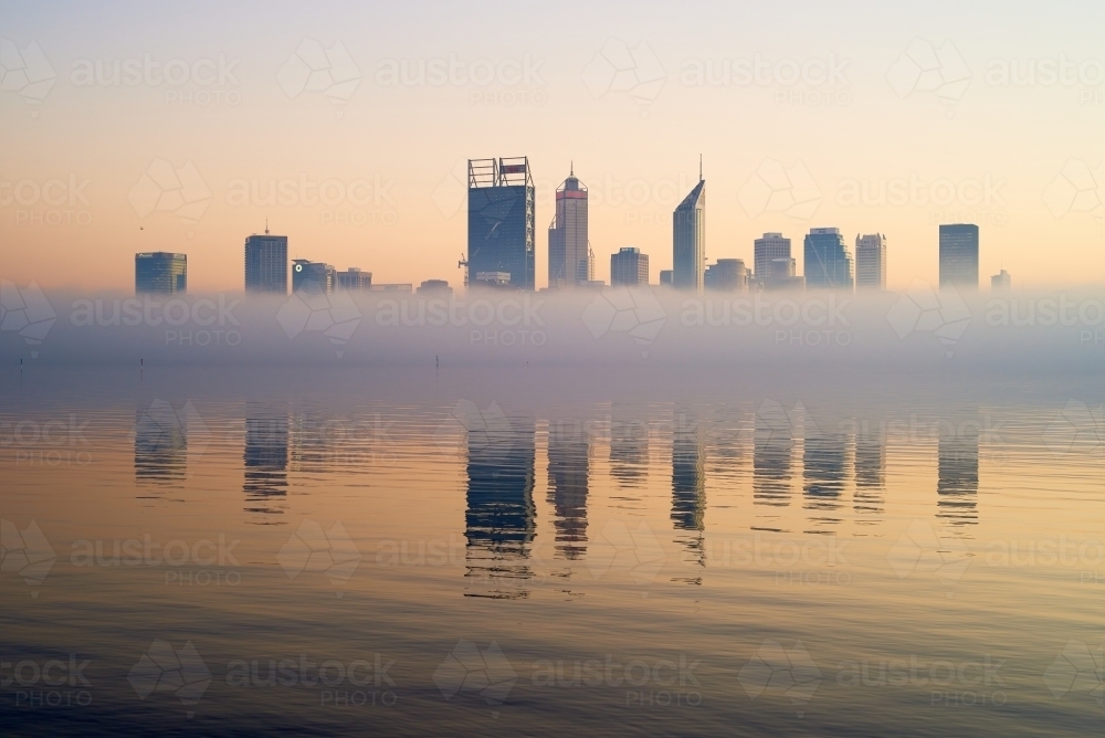 horizontal shot of Perth skyline at dawn with buildings reflected on misty water - Australian Stock Image