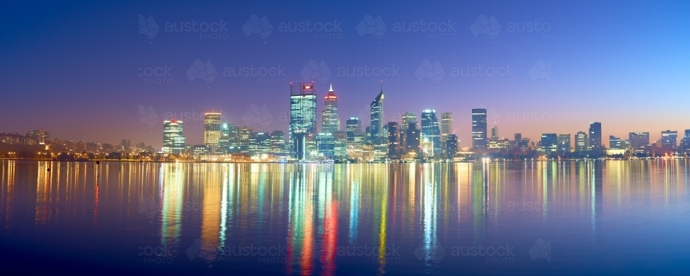 Panoramic shot of Perth skyline at dawn with colorful building lights reflected on water - Australian Stock Image