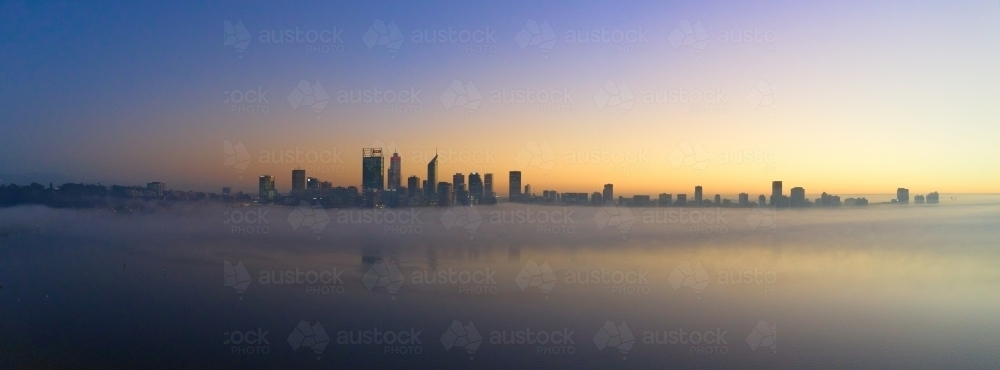 Panoramic shot of Perth skyline at dawn with misty atmosphere and some buildings reflected on water - Australian Stock Image