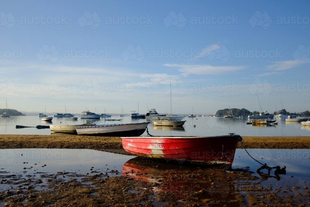 horizontal shot of several small boats docked in a low tide sea on a sunny day - Australian Stock Image