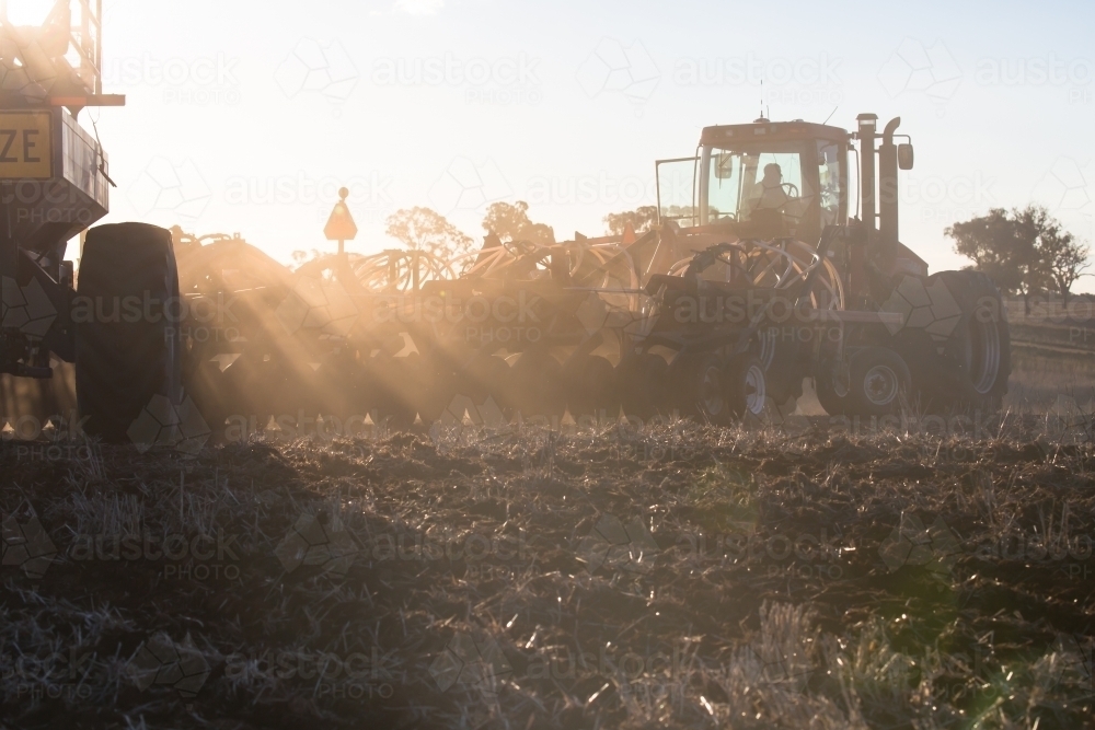 horizontal shot of silhouettes of tractors plowing soil in a sunny day - Australian Stock Image