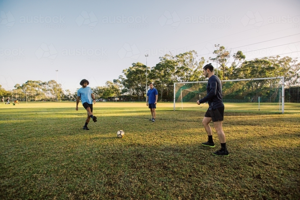 horizontal shot of three men playing soccer in the field on a sunny day with clear skies - Australian Stock Image