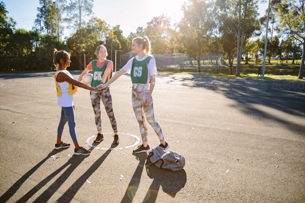 horizontal shot of three young smiling women in sports clothes stacking hands on top of each other - Australian Stock Image