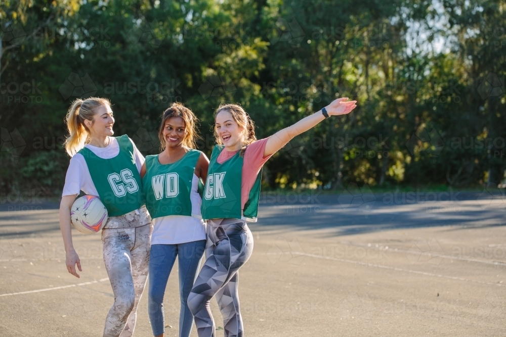 horizontal shot of three young smiling women in sports clothes with one holding a net ball - Australian Stock Image