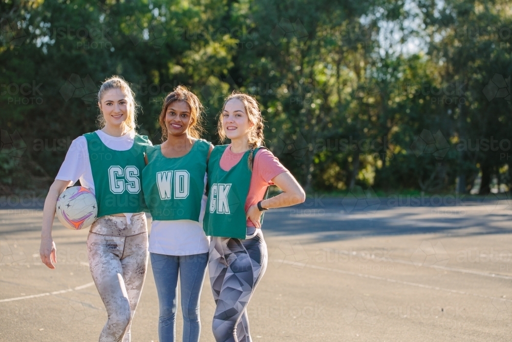 horizontal shot of three young smiling women in sports clothes with one holding a net ball - Australian Stock Image