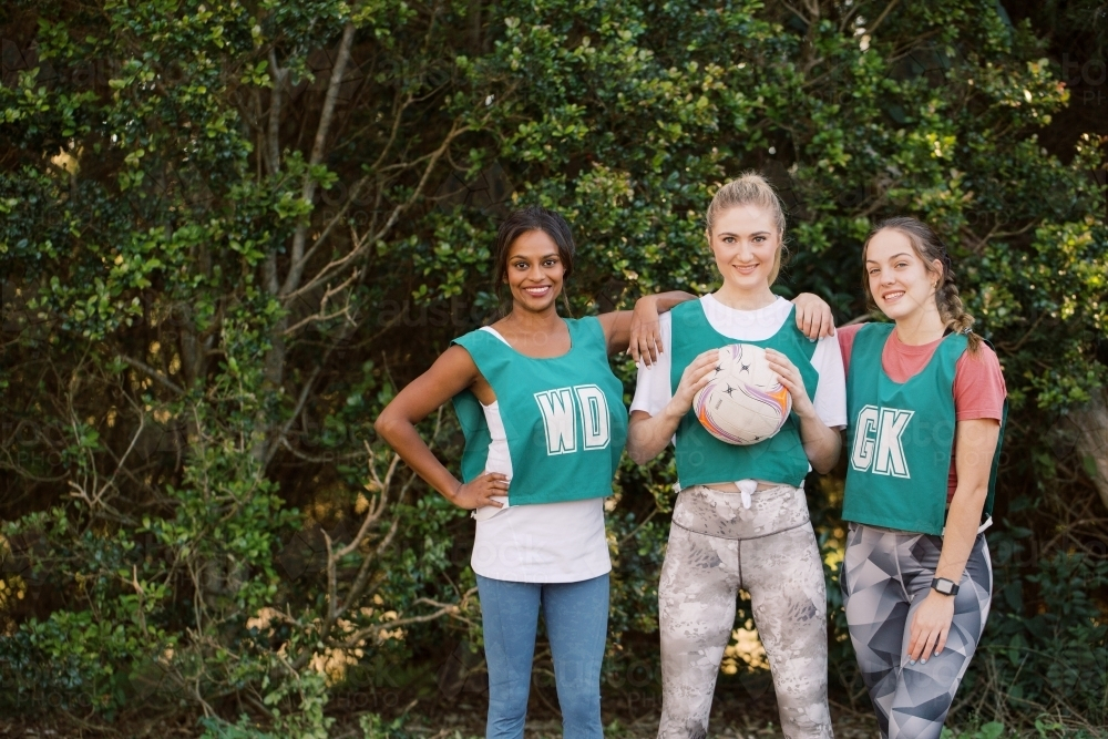 horizontal shot of three young sporty women posing outdoors with one holding a net ball - Australian Stock Image