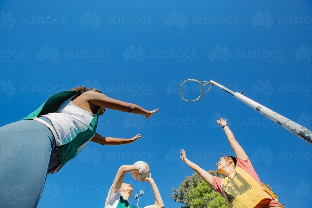 horizontal shot of three young women playing net ball on a sunny day with clear skies - Australian Stock Image