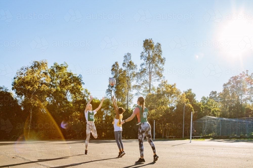 horizontal shot of three young women playing net ball outdoors on a sunny day - Australian Stock Image