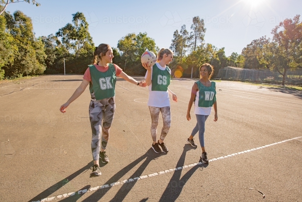horizontal shot of three young women smiling at each other with one girl holding a net ball - Australian Stock Image