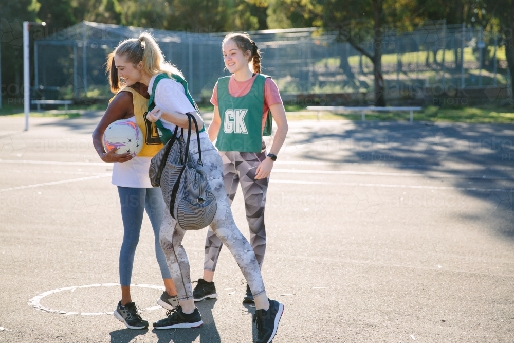 horizontal shot of three young women with two hugging each other on a sunny day with tree shadows - Australian Stock Image