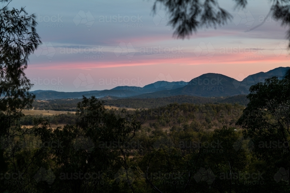 Horizontal shot of trees with mountain background under a pink sky - Australian Stock Image