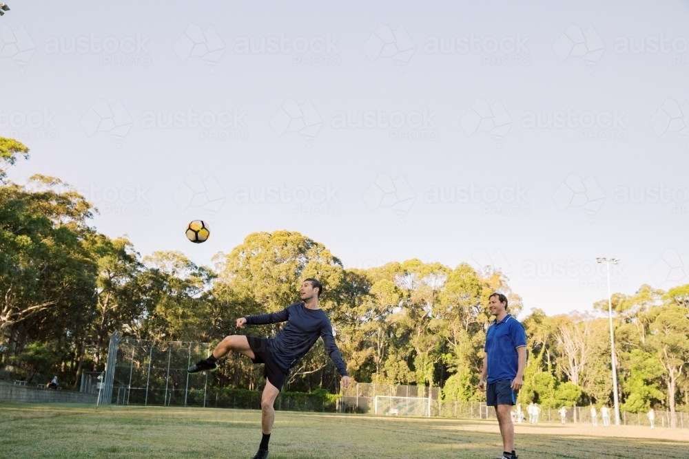 horizontal shot of two men playing soccer in the field with one man kicking the ball in mid air - Australian Stock Image