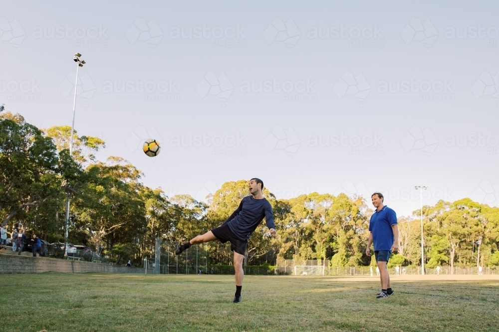 horizontal shot of two men playing soccer in the field with one man kicking the ball in mid air - Australian Stock Image