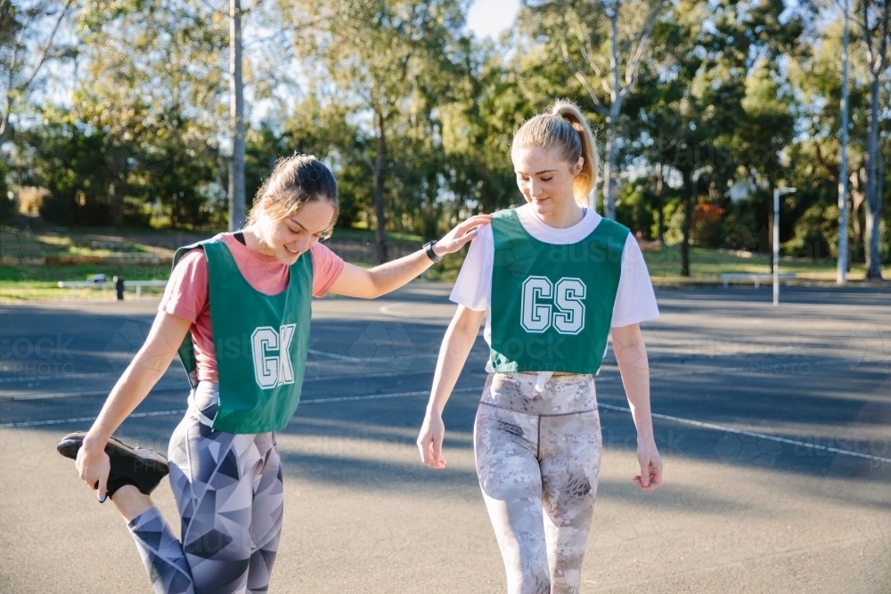 horizontal shot of two young women with one stretching her leg while holding on the shoulder - Australian Stock Image
