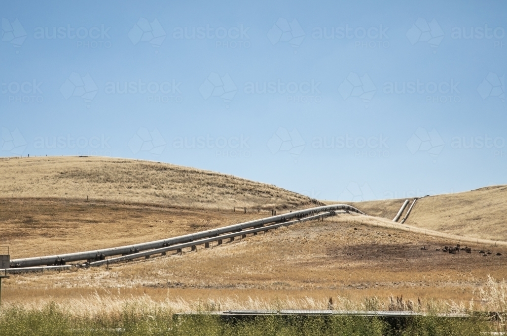 Horizontal shot of waterpipes on hill through farmland - Australian Stock Image