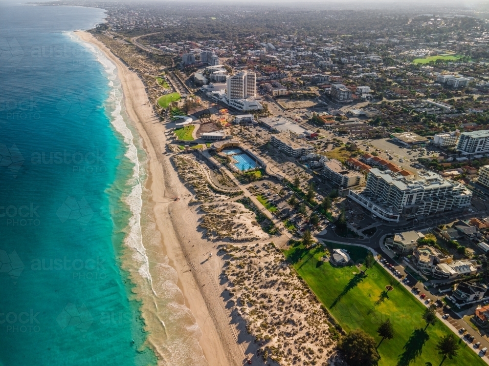 horizontal shot of white sand shoreline, green grass ocean water, trees and buildings - Australian Stock Image