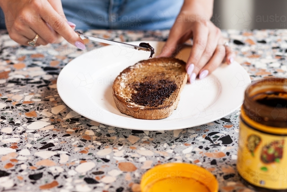 horizontal shot of woman making vegemite toast on a table with color design - Australian Stock Image