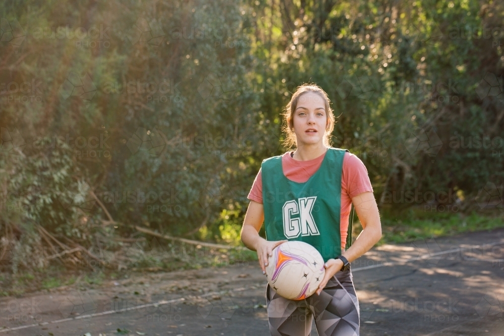 horizontal shot of young woman in sports clothes holding a net ball with two hands on a sunny day - Australian Stock Image
