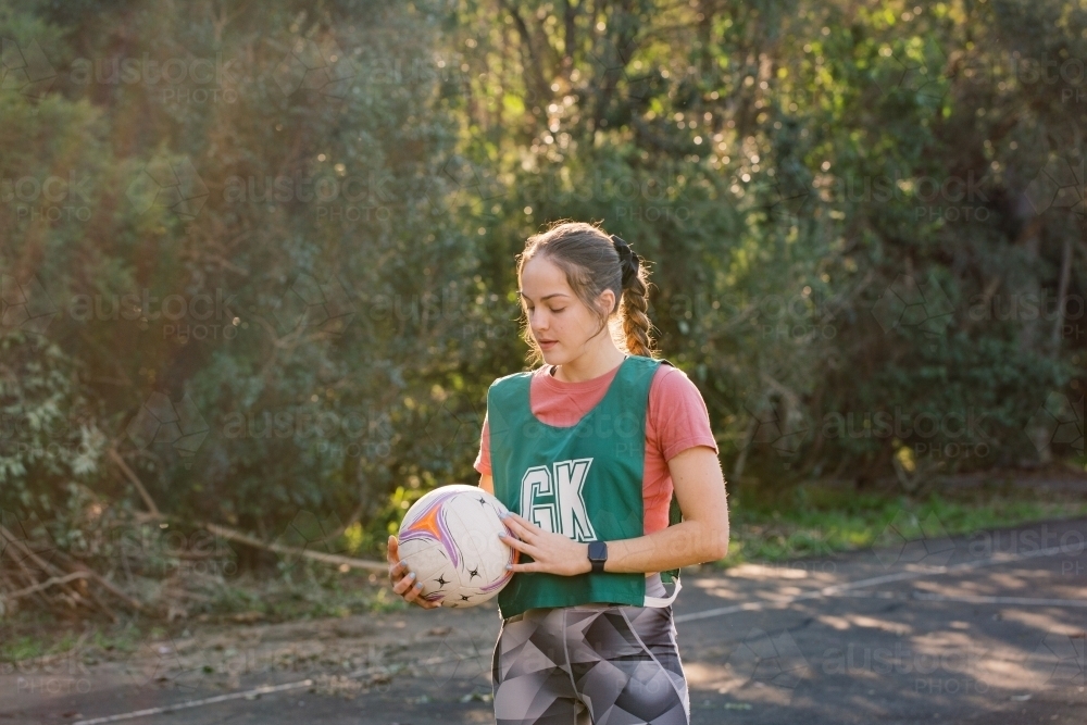 horizontal shot of young woman in sports clothes holding a net ball with two hands on a sunny day - Australian Stock Image