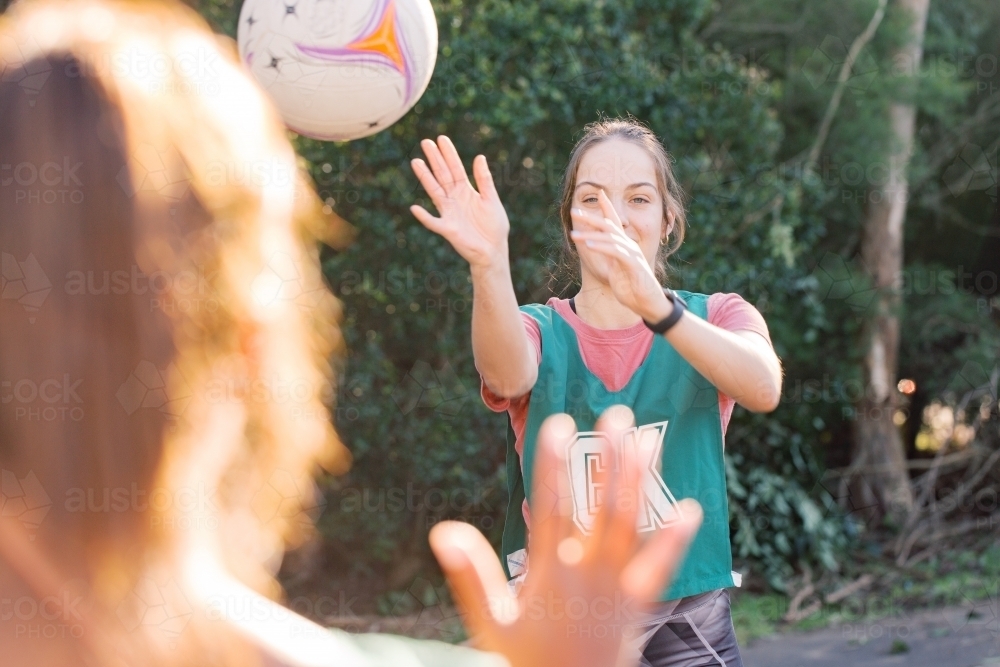 horizontal shot of young woman throwing a net ball to another woman blurred in the foreground - Australian Stock Image