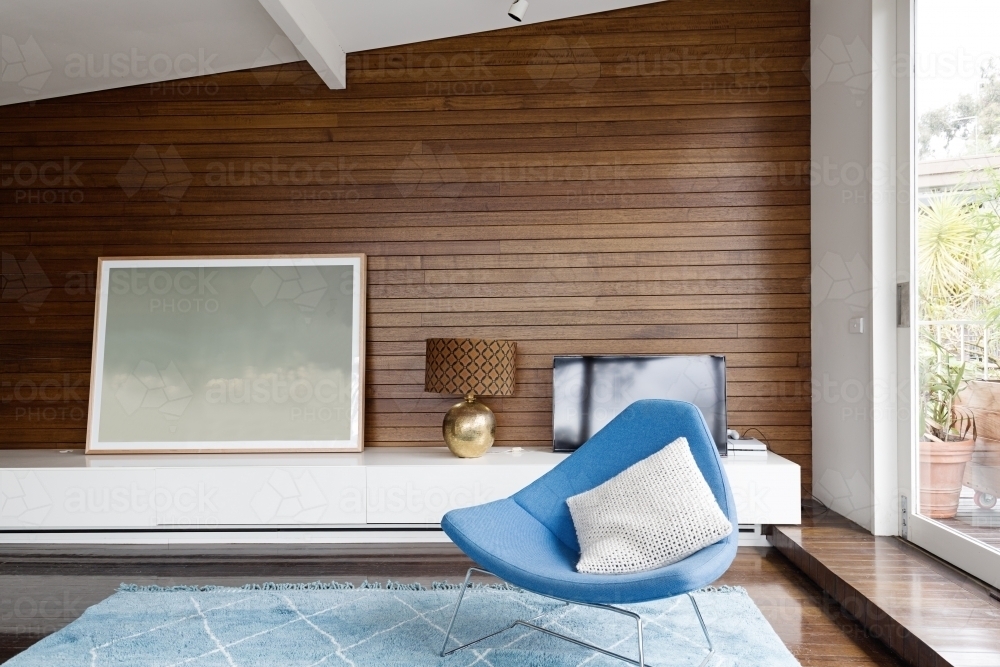 Horizontal wood panelling and blue chair in mid century living room - Australian Stock Image