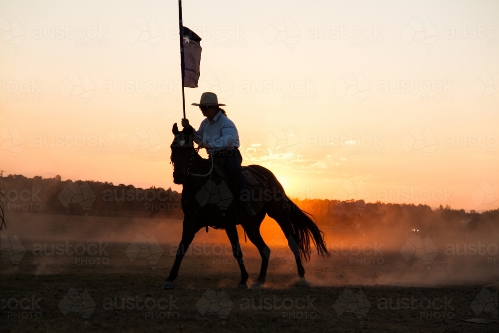 Horse and rider silhouetted at sunset riding through dust - Australian Stock Image